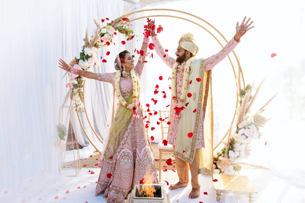 Intimate backyard South Asian wedding with gold hoop backdrop with pampas grass and suspended red rose petals | PartySlate
