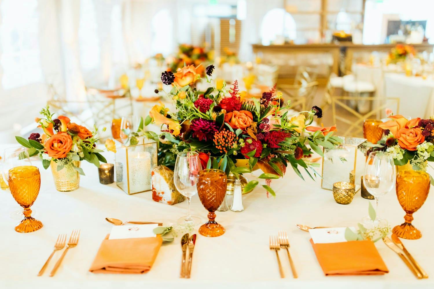 Fall-hued wedding floral centerpiece with amber glassware and copper-hued napkins and cutlery | PartySlate