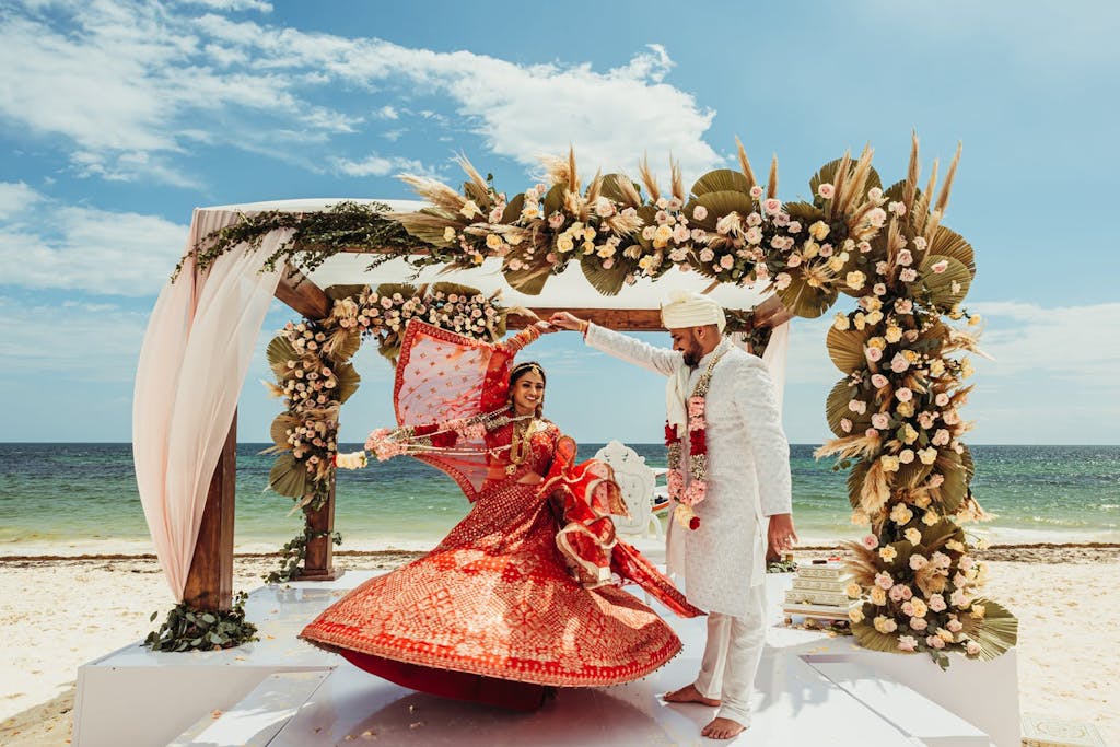Bride and groom dance in front of wooden mandap with white drapery and tropical floral designs at Cancún destination wedding | PartySlate