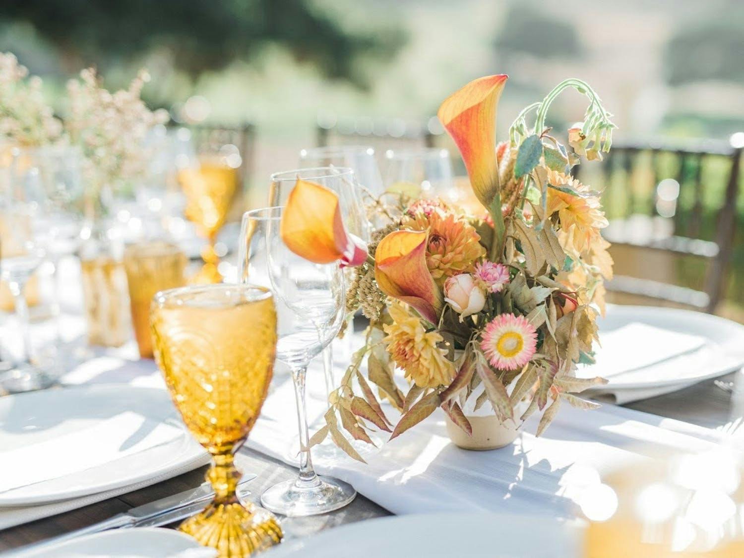 Wedding reception table with gold glassware and gold-hued fall floral centerpiece with organic fading leaves | PartySlate