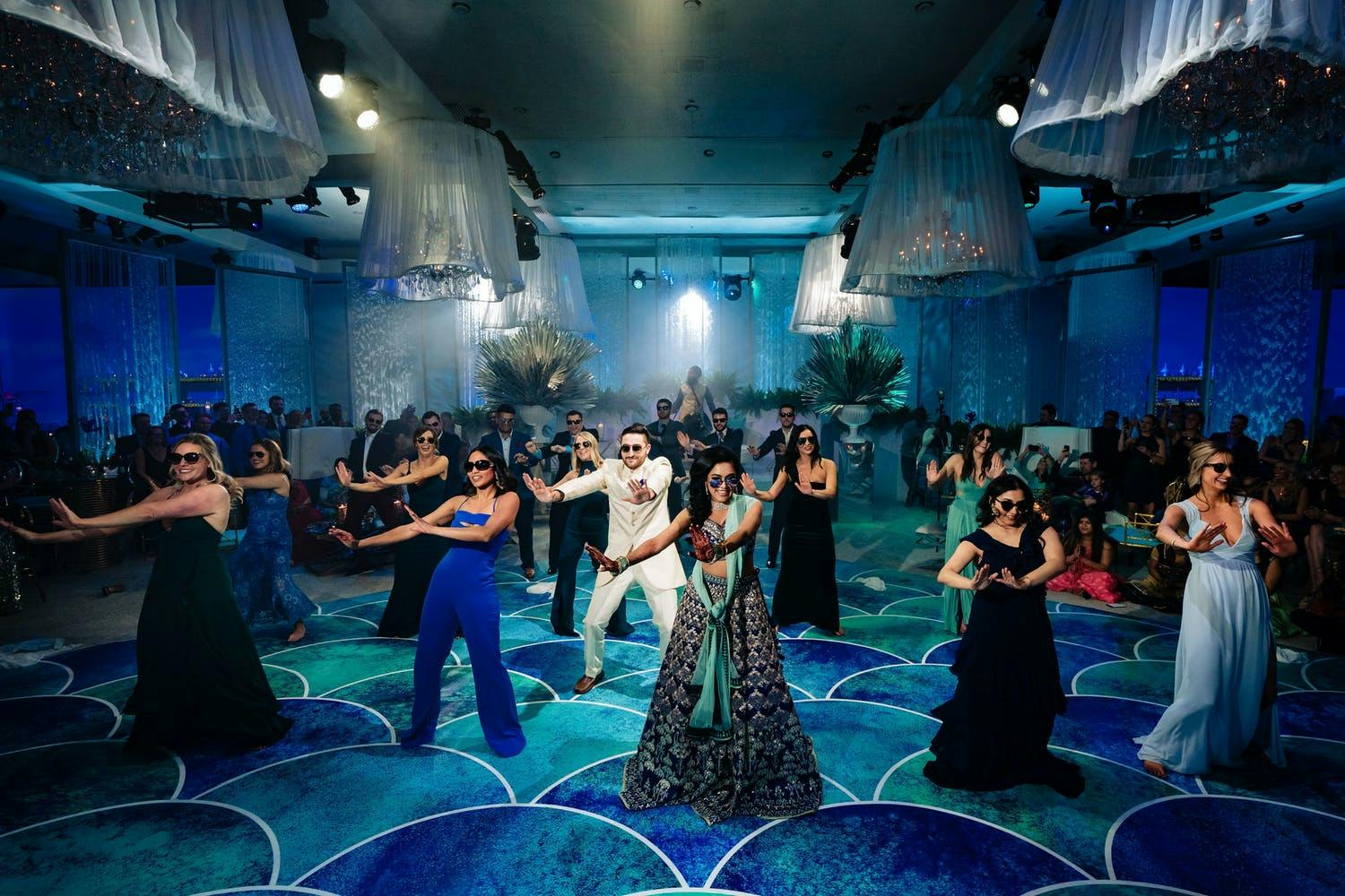 South Asian choreographed dance on blue and green ocean-like dance floor with vibrant blue uplighting | PartySlate