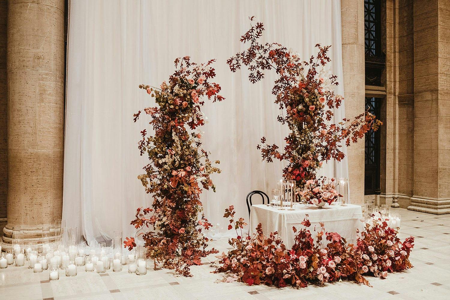 Sweetheart table with pink and champagne-hued floral centerpieces and asymmetrical backdrop | PartySlate
