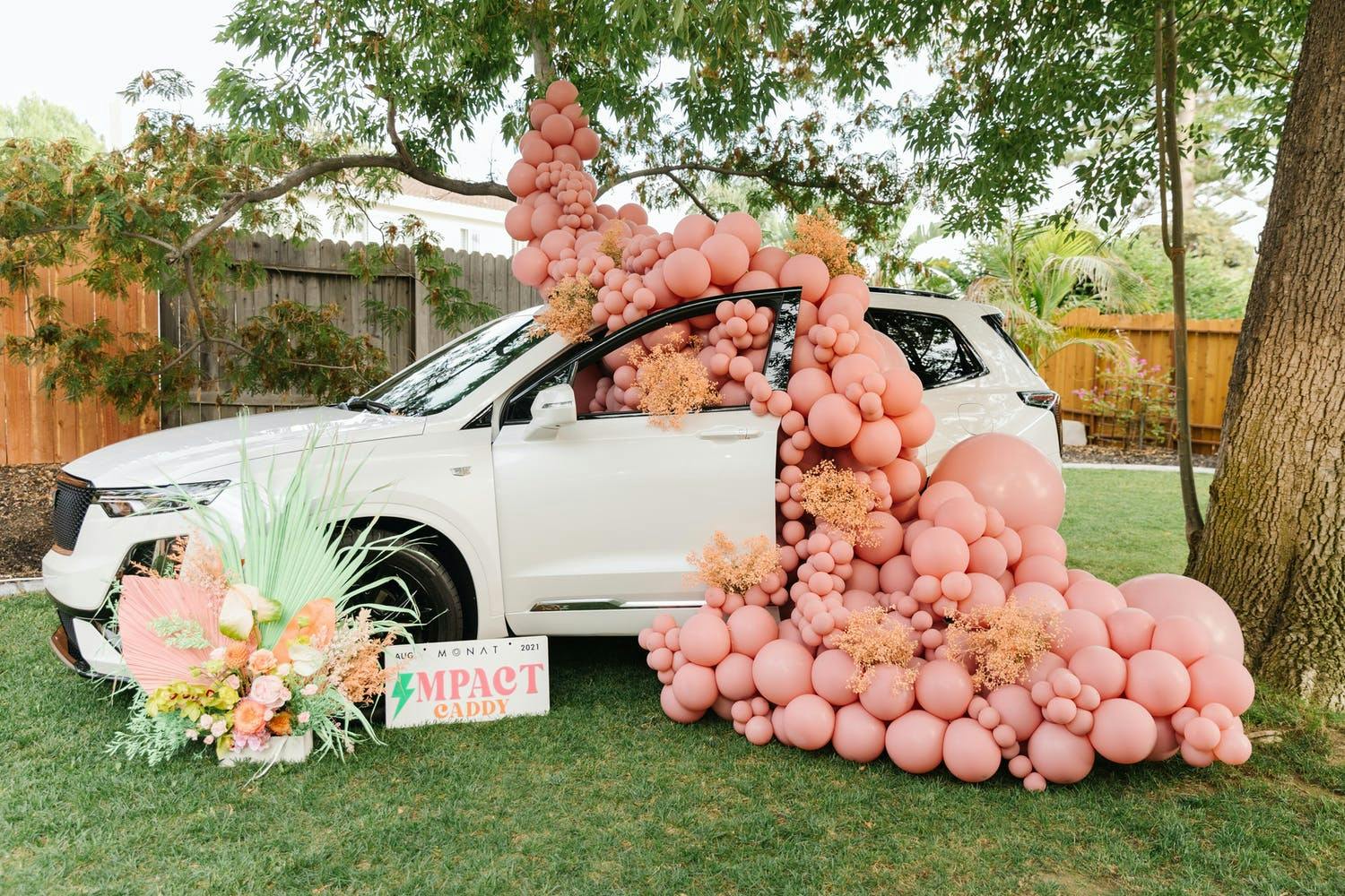 Backyard corporate dinner party with white SUV overflowing with peachy-pink matte balloons | PartySlate