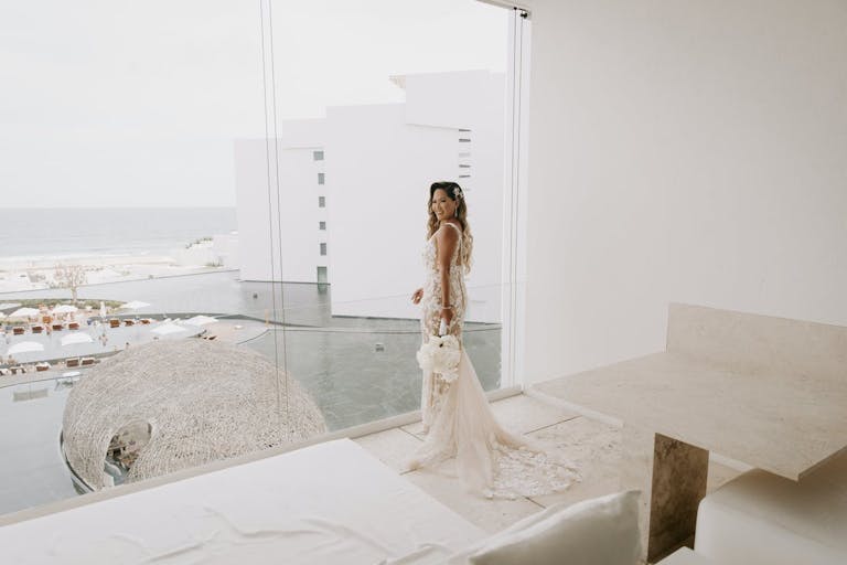 Bride Standing in Bridal Suite Overlooking the Beach Front Honeymoon Destination | PartySlate