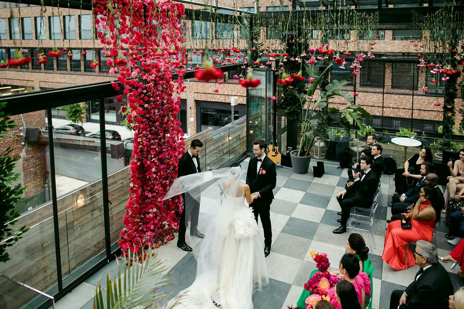 Wedding at 74Wythe with upended red floral ceiling décor and wedding backdrop of waterfall-style red blooms | PartySlate