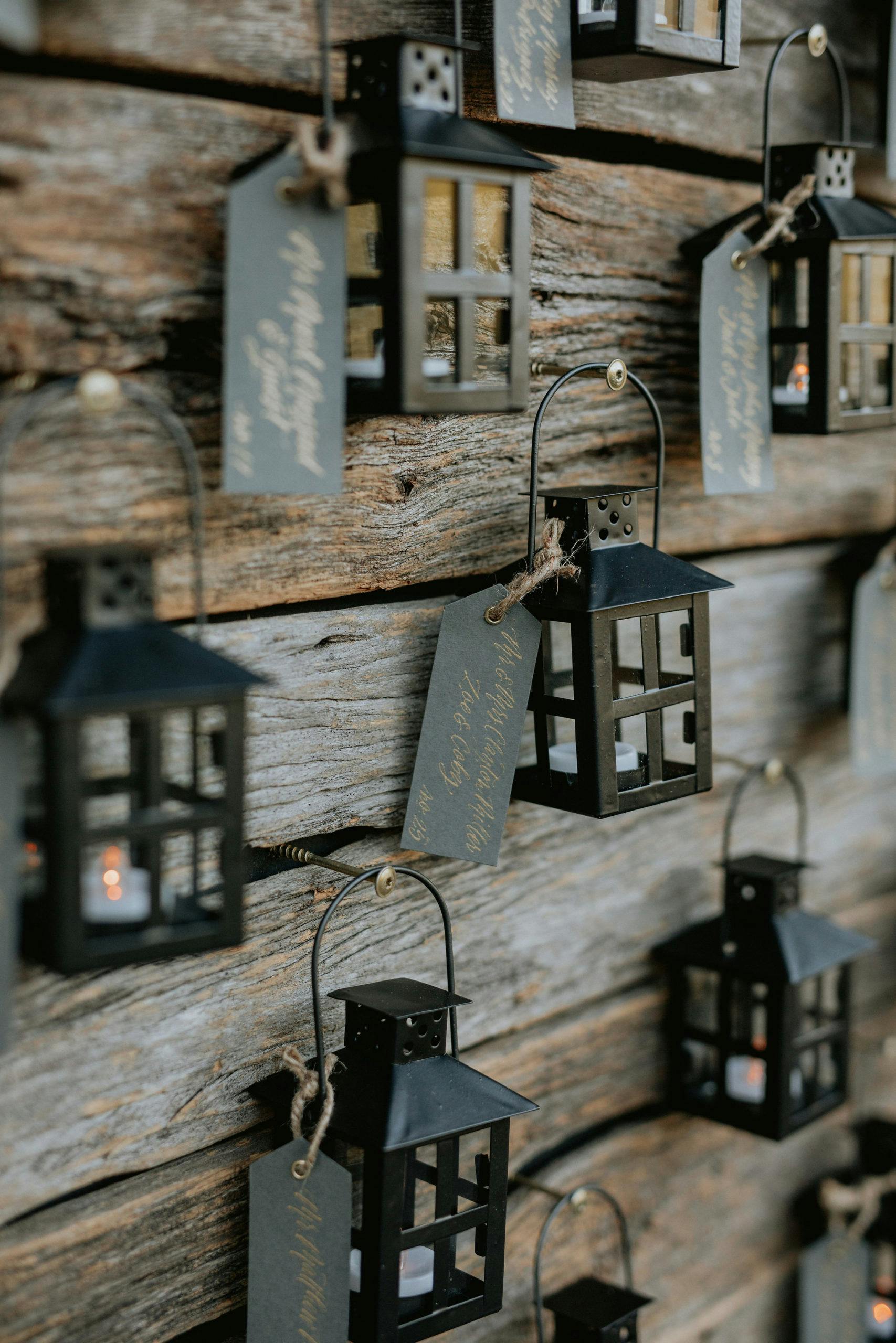 Mini black lanterns place cards hanging on a wooden wall for a fall wedding | PartySlate