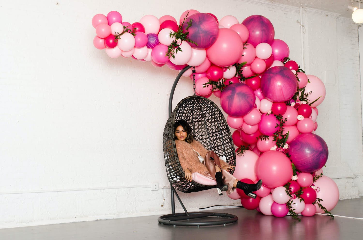 Woman sits on swing photo op with cascade of hot pink balloons | PartySlate