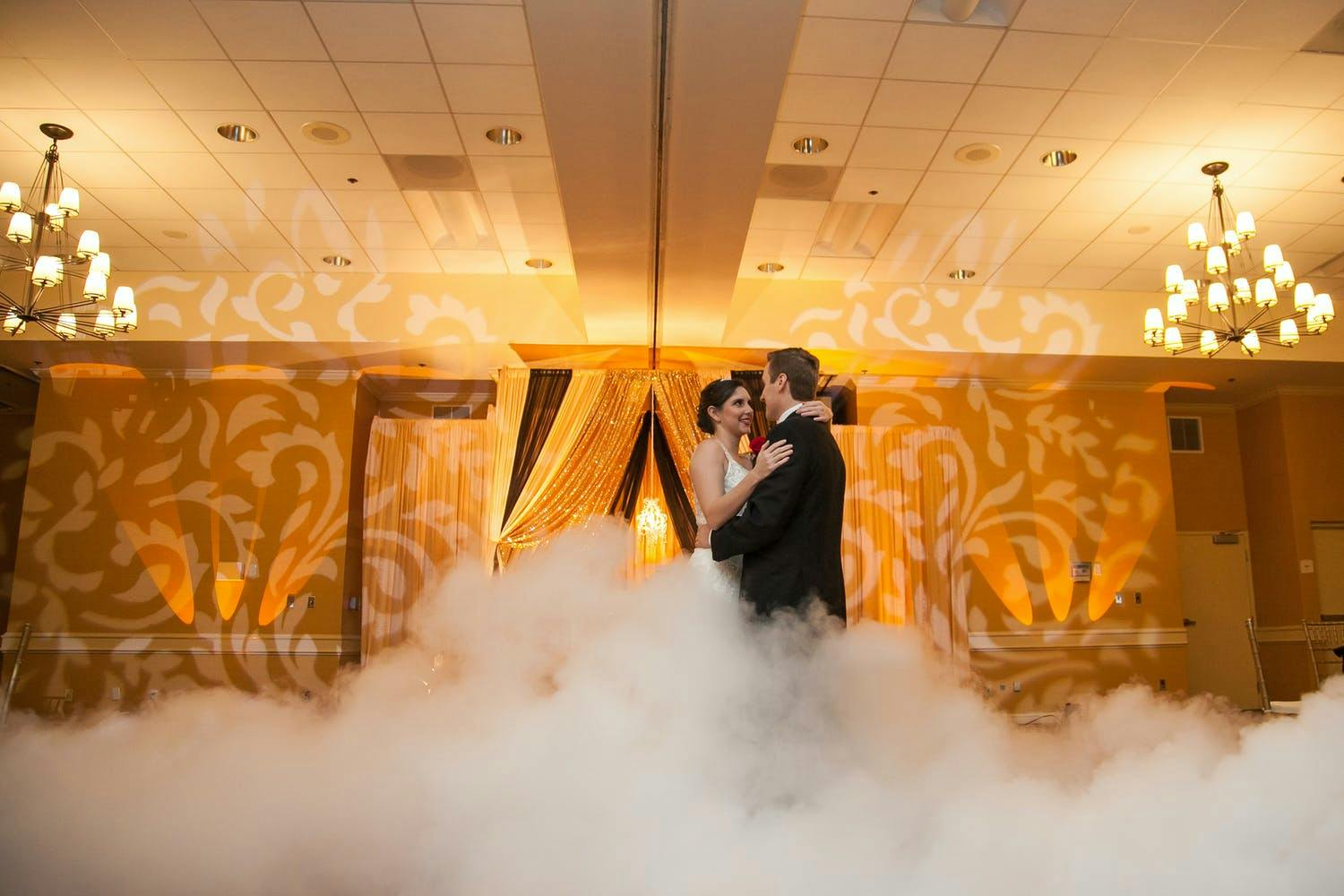 Couple dance in fog with golden paisley-patterned lighting projected behind them | PartySlate