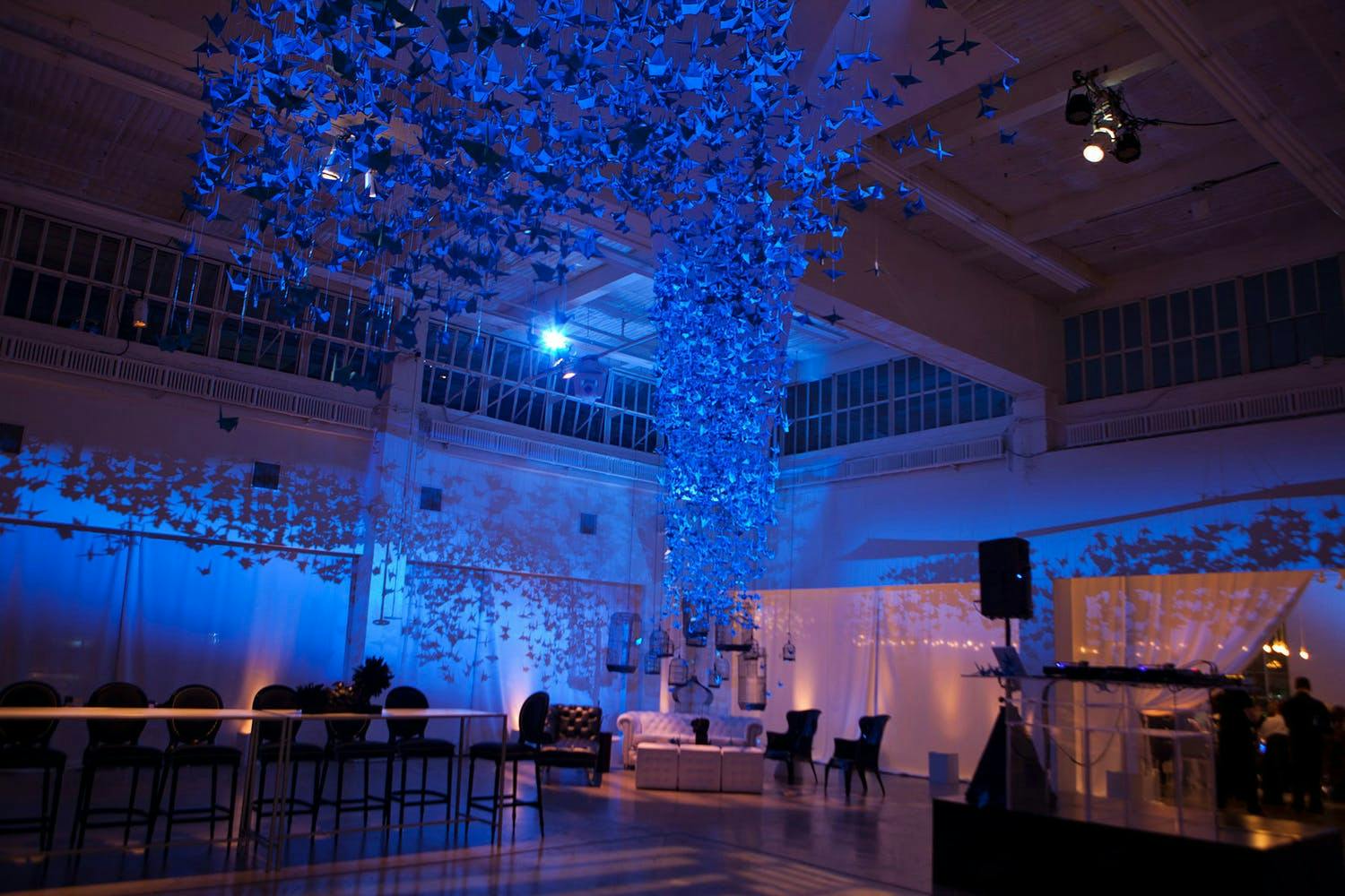 Ceiling installation of bright blue cranes against blue uplighting at wedding | PartySlate