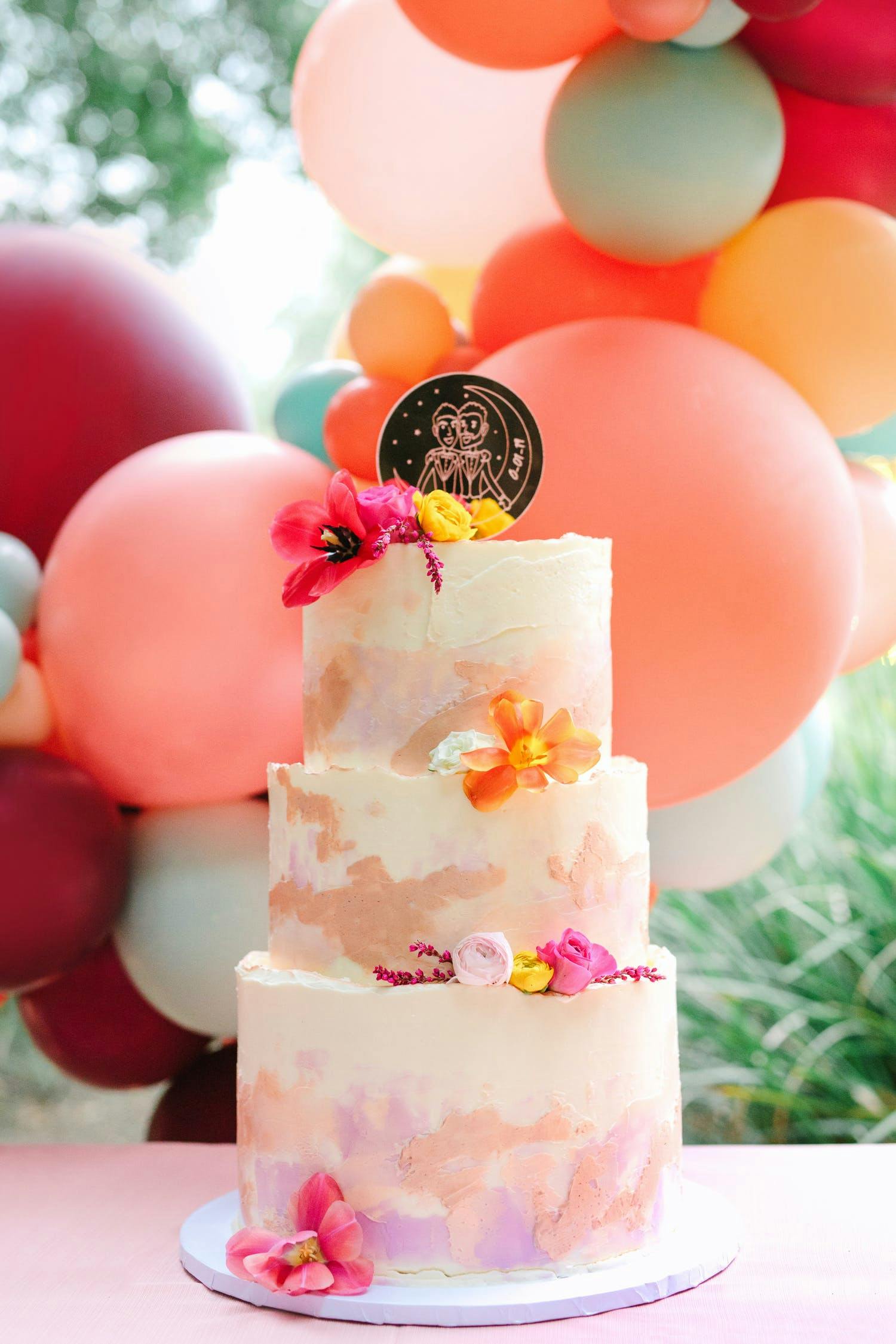 Wedding cake with pink and red balloons in background | PartySlate