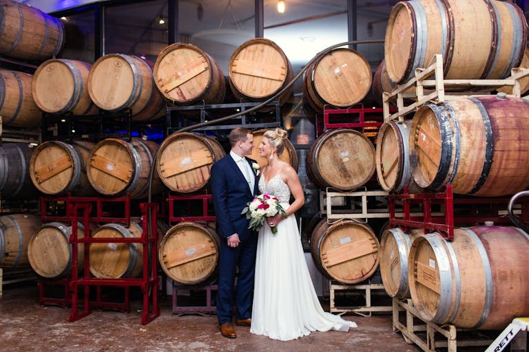 Couple Standing In Wine Cellar in Wedding dress and Tux with Bouquet of Flowers | PartySlate