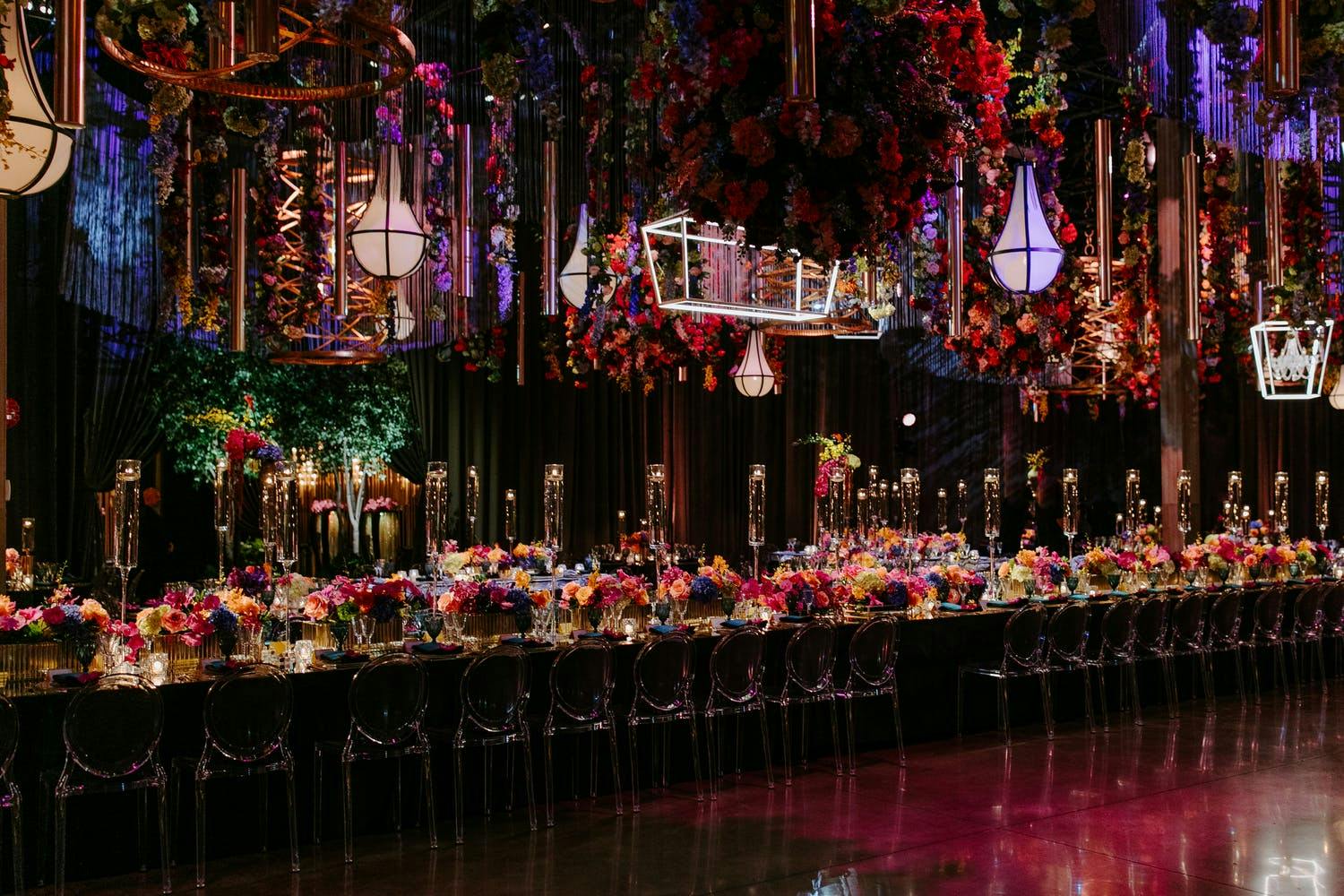 Vibrant wedding reception with colorful flowers and geometric ceiling decorations and lighting | PartySlate