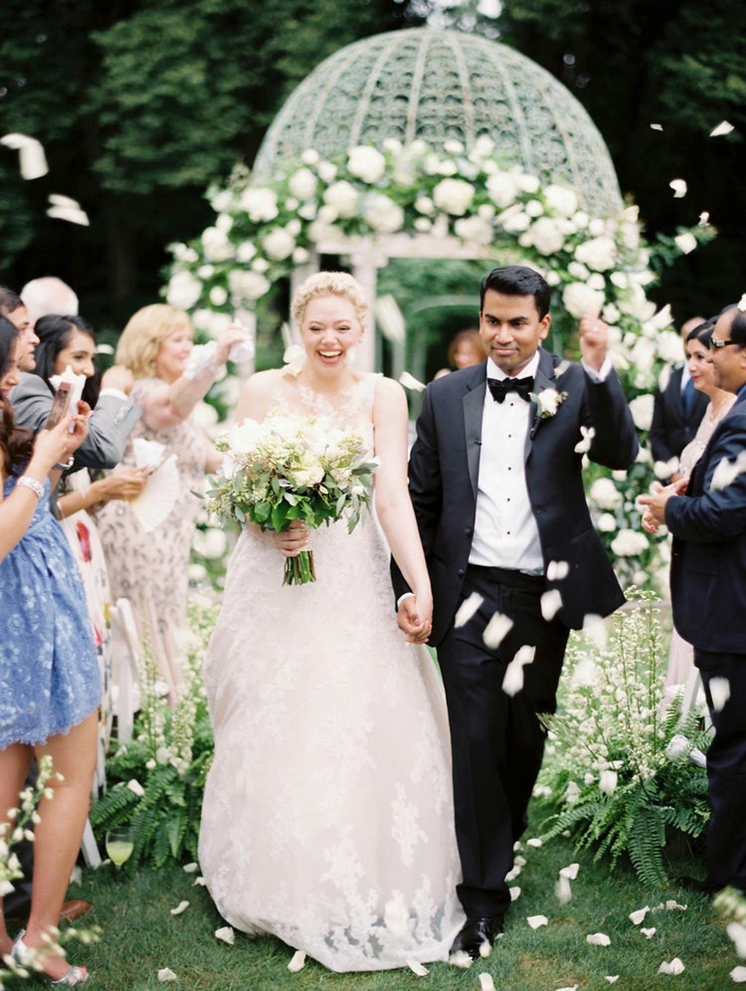 Recessional walk at outdoor wedding with white gazebo covered in white flowers | PartySlate