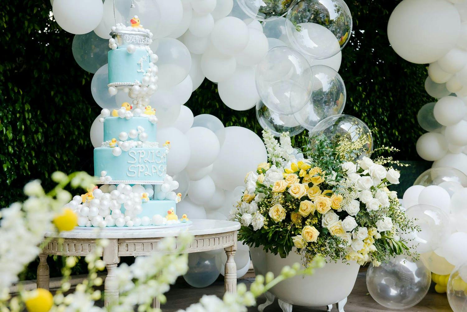 Rubber Ducky Themed Party With Blue and Yellow Tiered Cake and White and Clear Bubble Balloons and Fresh Yellow and Green Florals | PartySlate