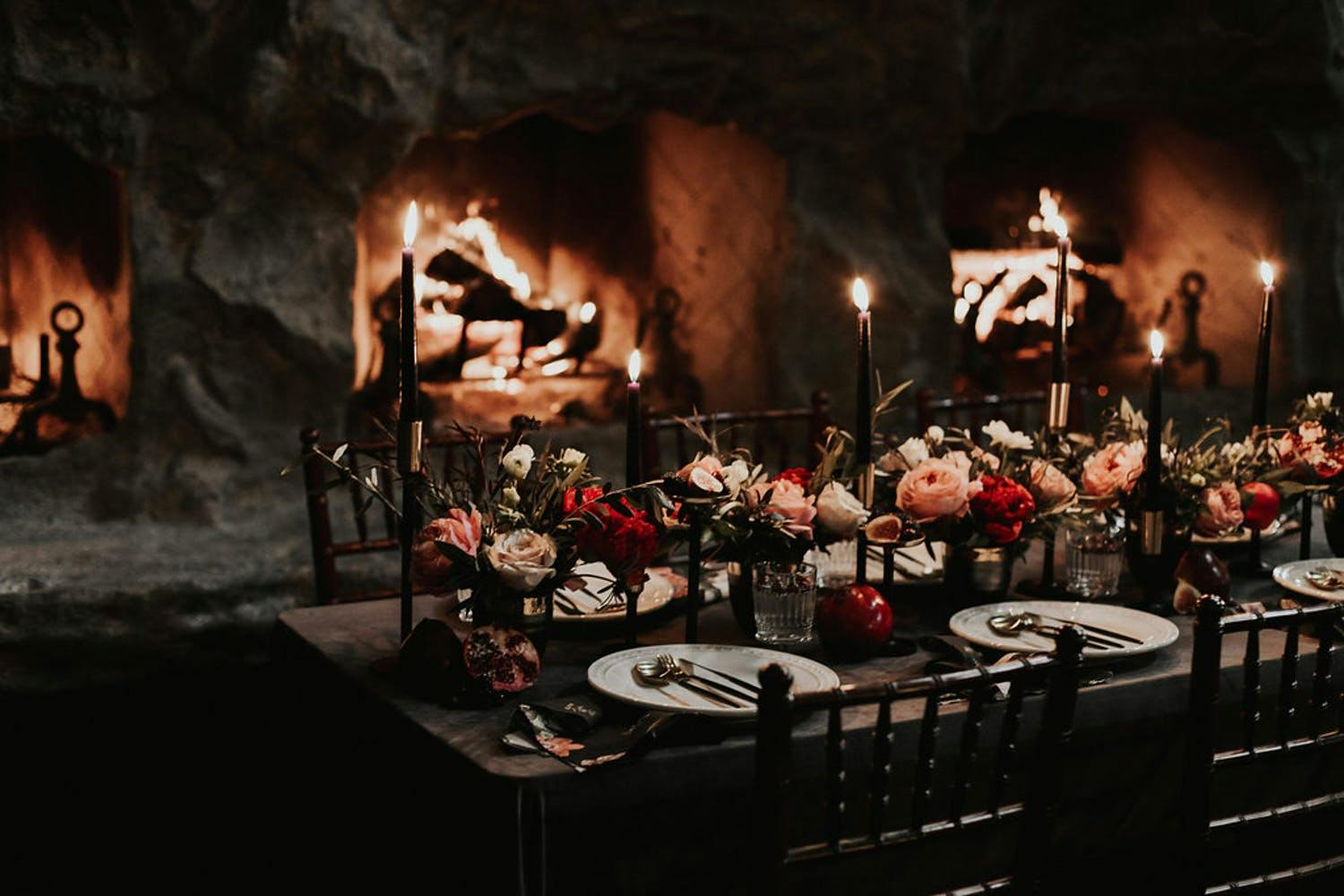 Candlelit winter wedding table with roses and black tapered candles set against consecutive fireplaces | PartySlate