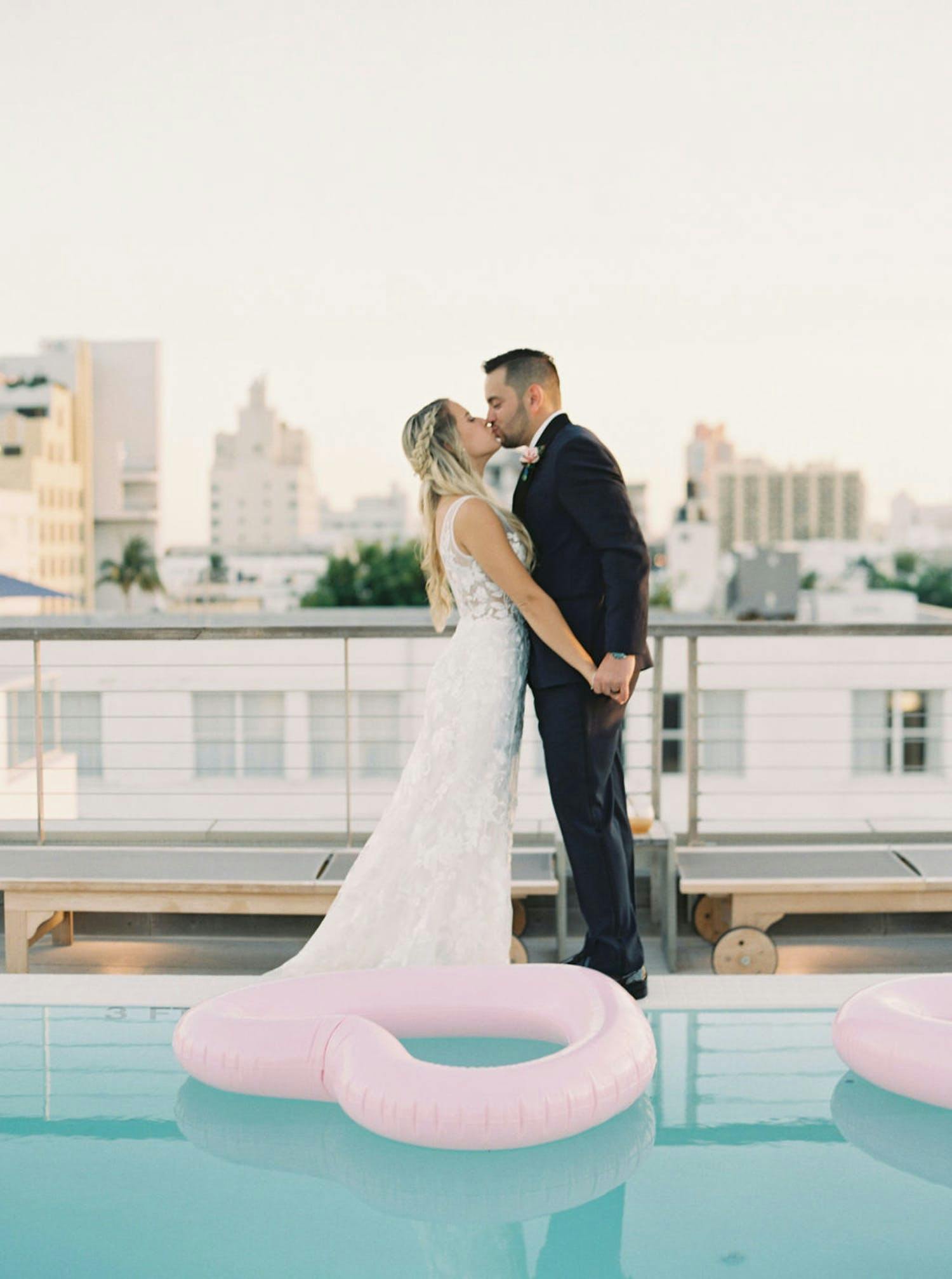 Couple kiss on rooftop venue in front of pool with heart-shaped inflatables | PartySlate