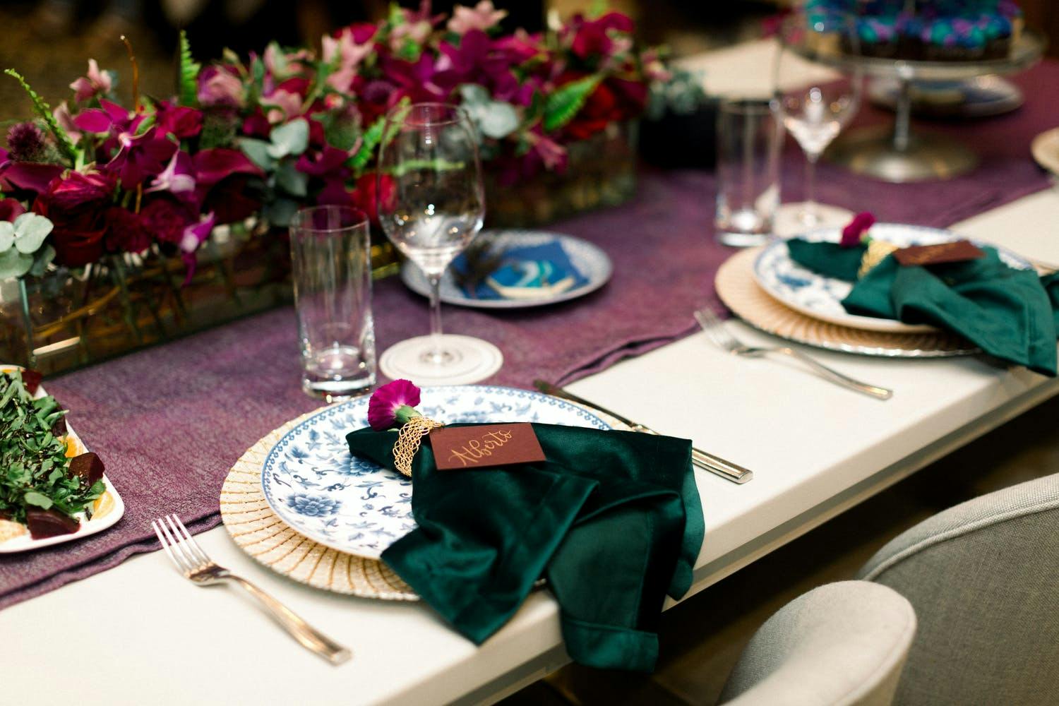 Wedding table décor with pink flowers and evergreen velvet napkins | PartySlate