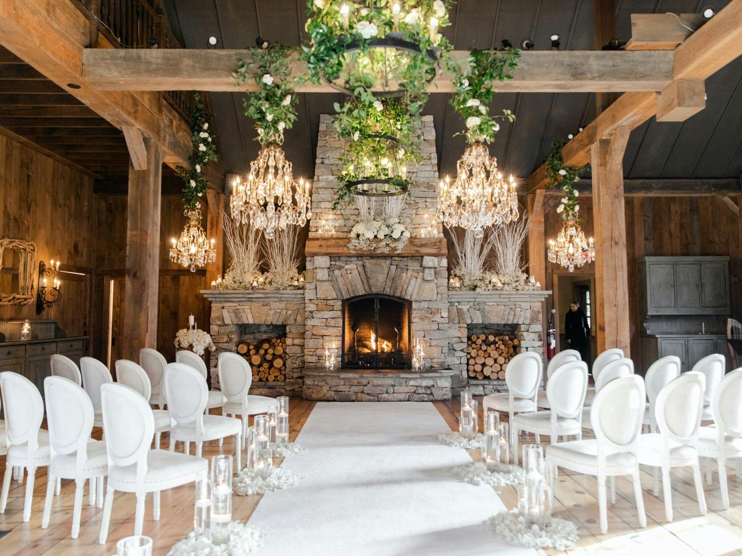 Wedding ceremony with two-story stone fireplace, greenery, and glittering chandeliers | PartySlate