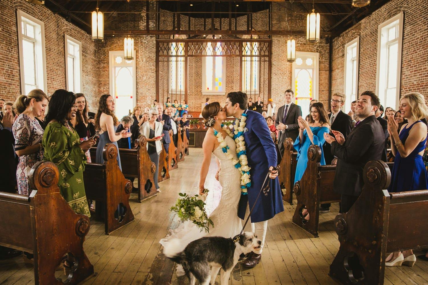 Bride and groom kiss, with dog, at multicultural wedding ceremony in church | PartySlate