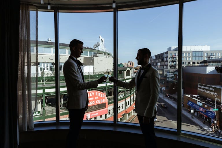 Two Grooms Making A Toast In Front of Window that Looks Out To Wrigley Field at Hotel Zachary | PartySlate