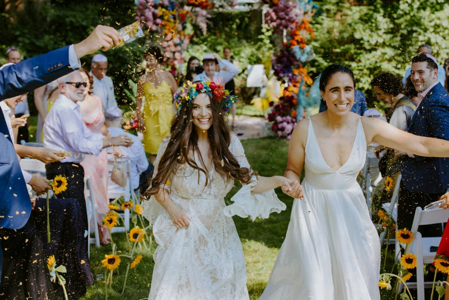 Two women walk down aisle during recessional at outdoor garden wedding | PartySlate
