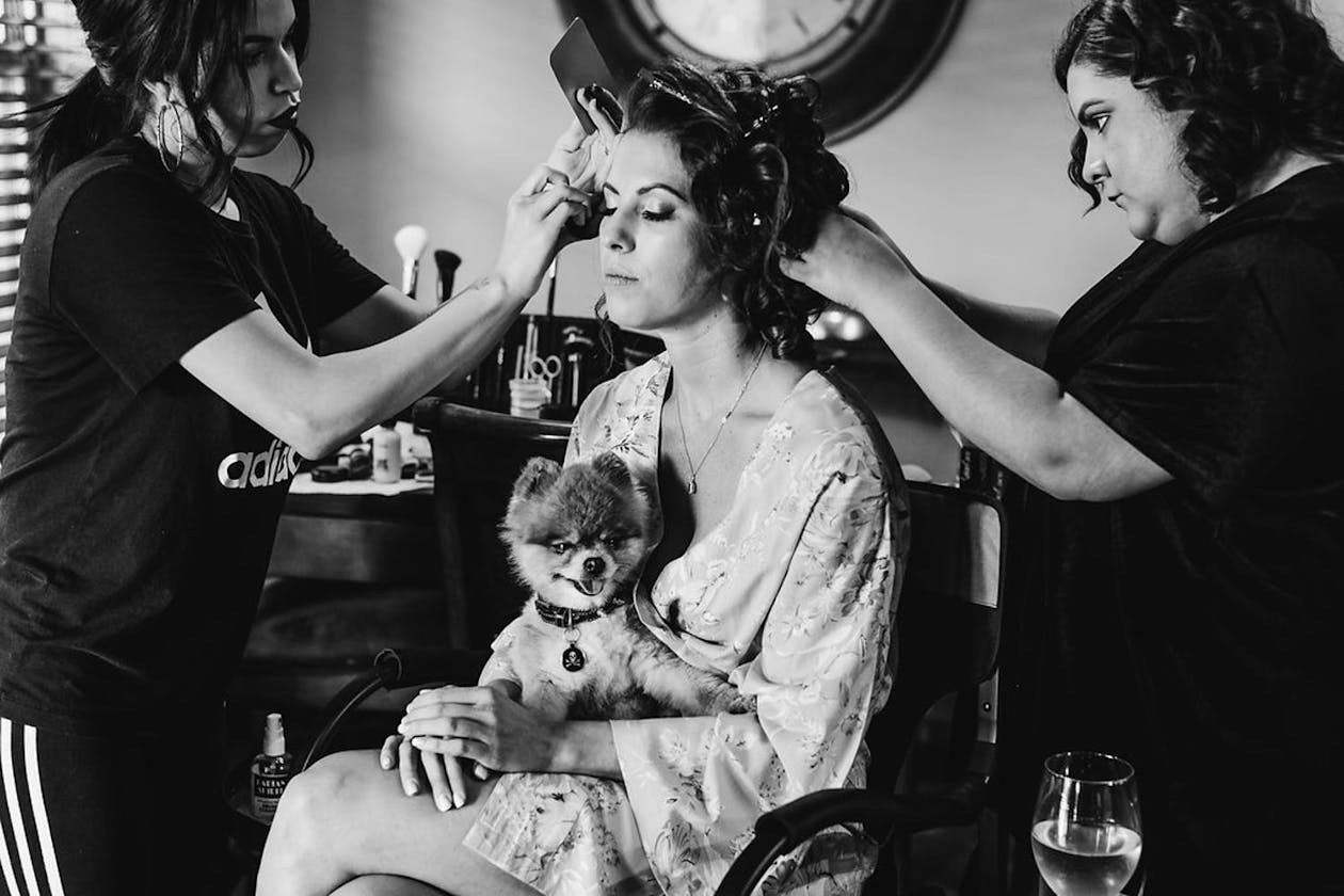 bride getting makeup and hair done with dog on lap | PartySlate