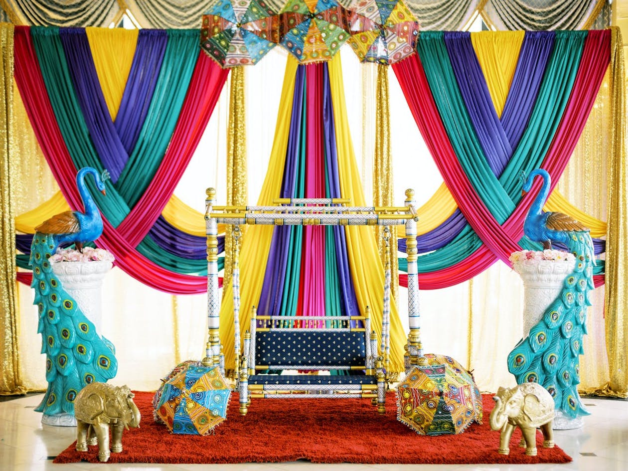 Jhula against bold yellow, blue, red, and purple drapery with umbrella décor | PartySlate