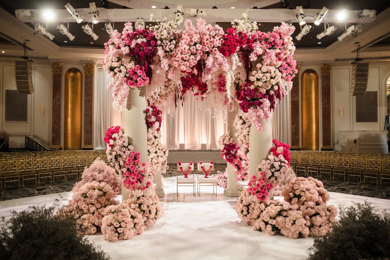 Ballroom Indian wedding mandap with white poles and lavish pink ombré flowers | PartySlate