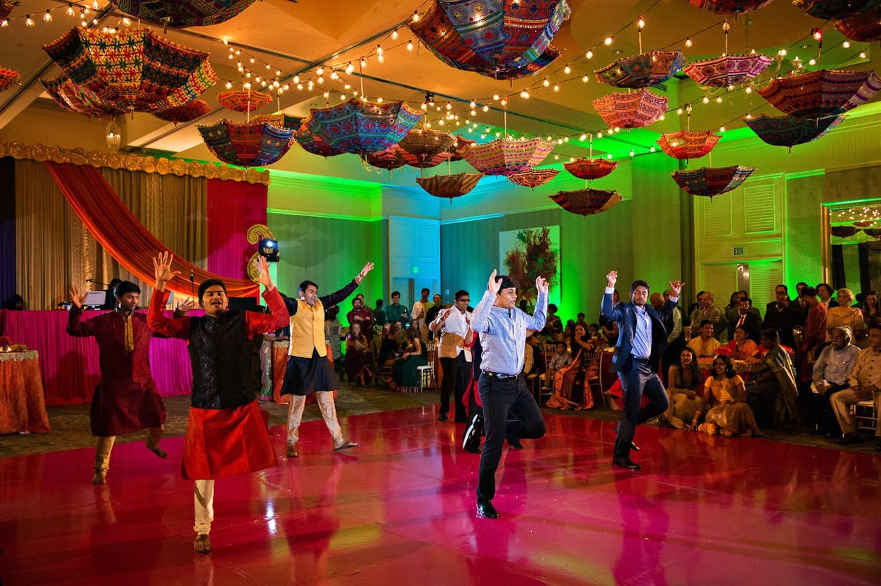 People dance on shiny pink dance floor under umbrella ceiling décor at Indian wedding sangeet | PartySlate