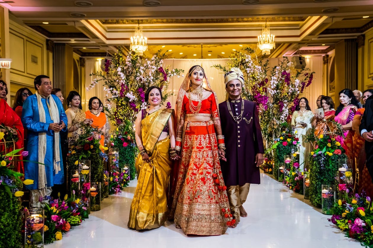 Vibrant Indian Wedding aisle with tall greenery and colorful blooms | PartySlate