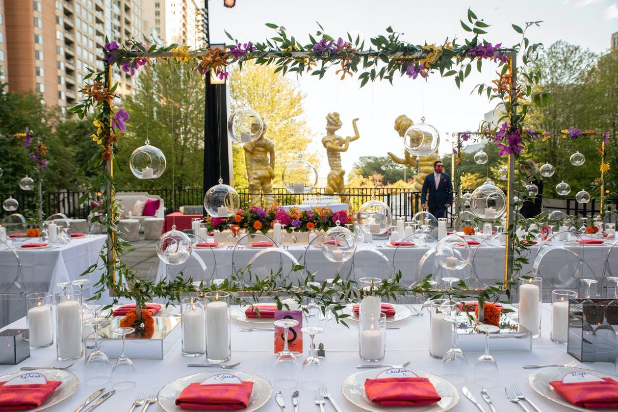 Outdoor Indian wedding reception with white linen tablescapes with red napkins and elevated greenery centerpieces | PartySlate