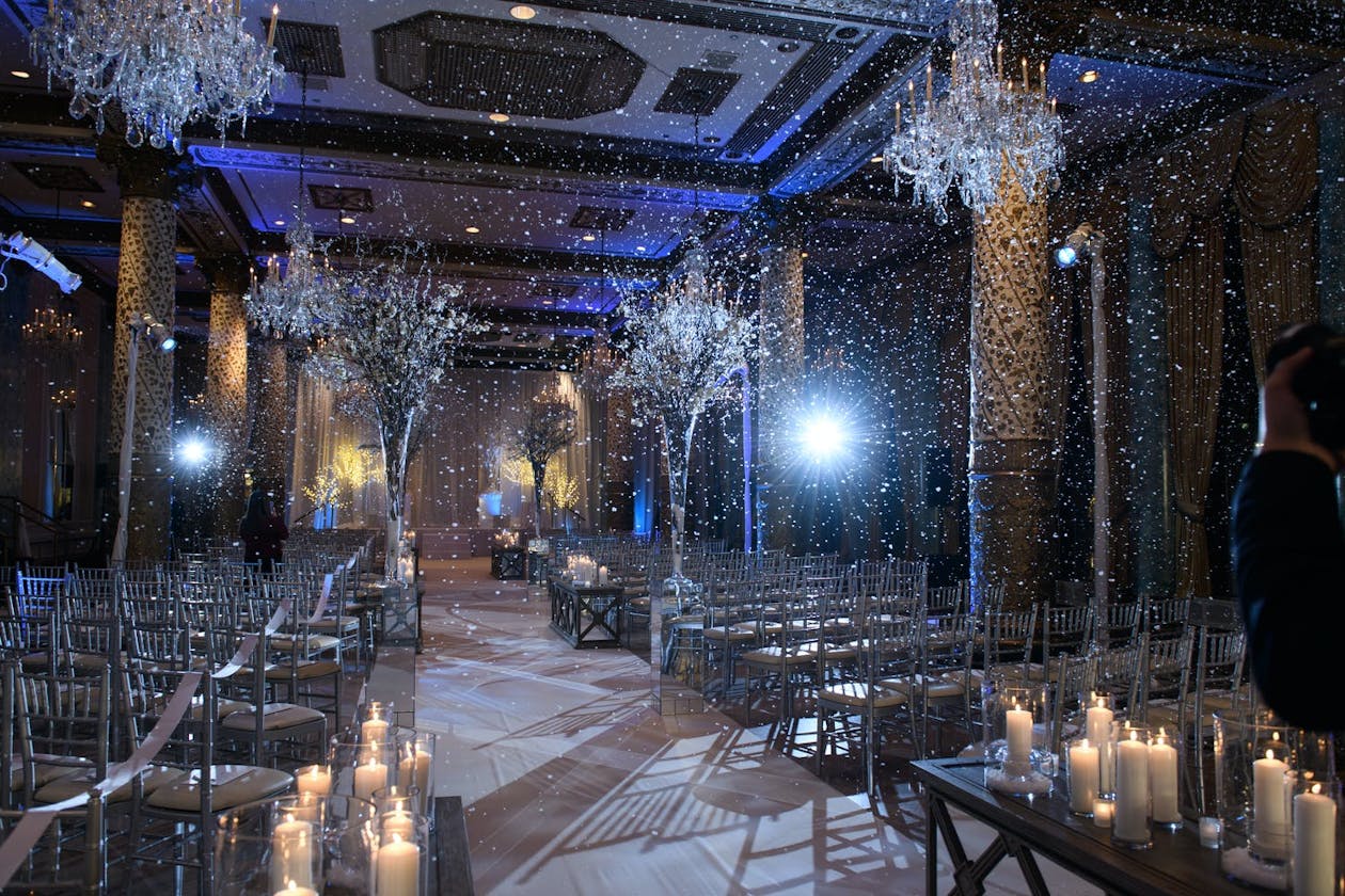 Winter wonderland wedding ceremony with falling snow and blue uplighting | PartySlate