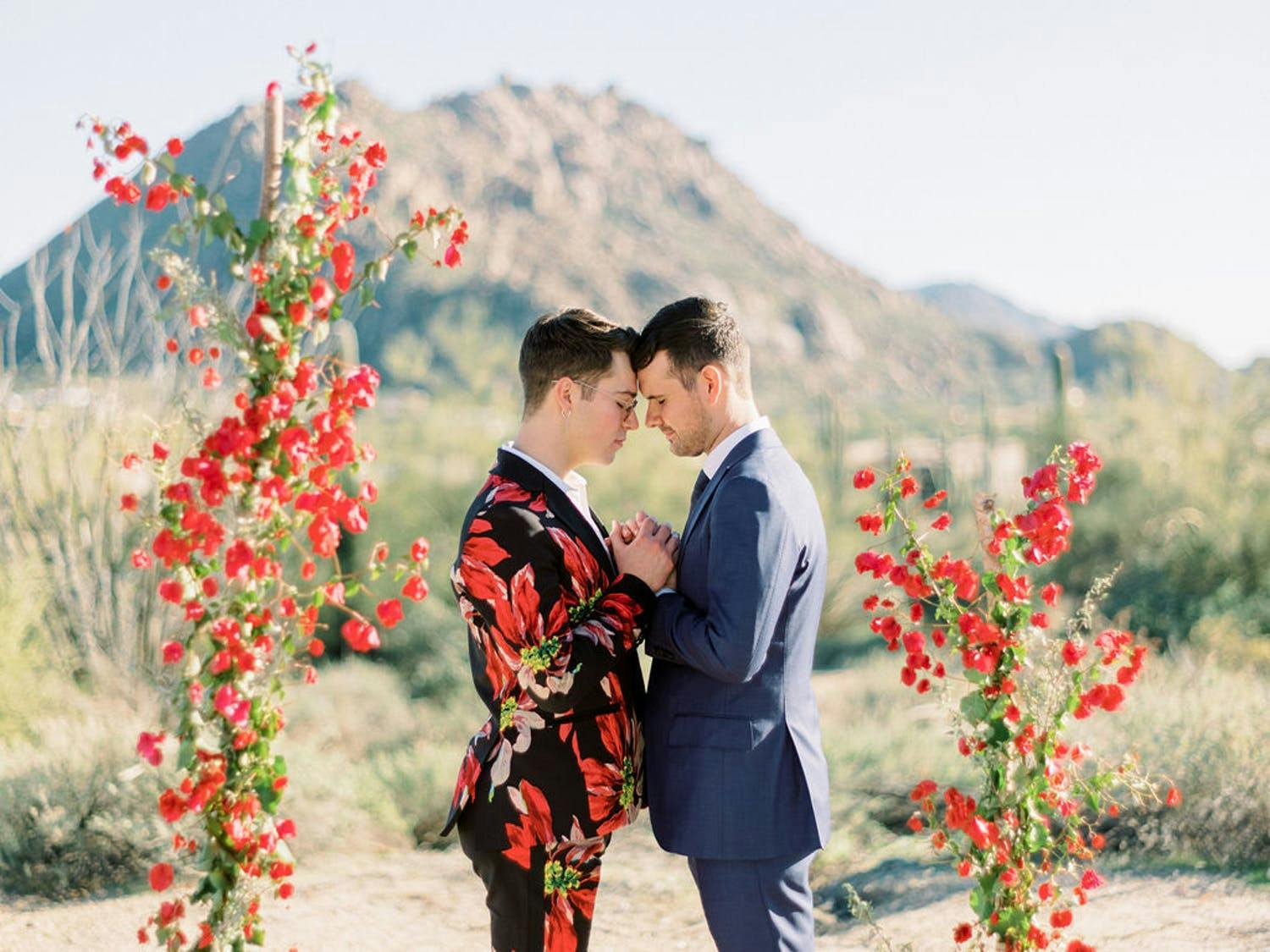 Two groom touch foreheads between Bougainvillea vines at desert wedding in Scottsdale, AZ | PartySlate