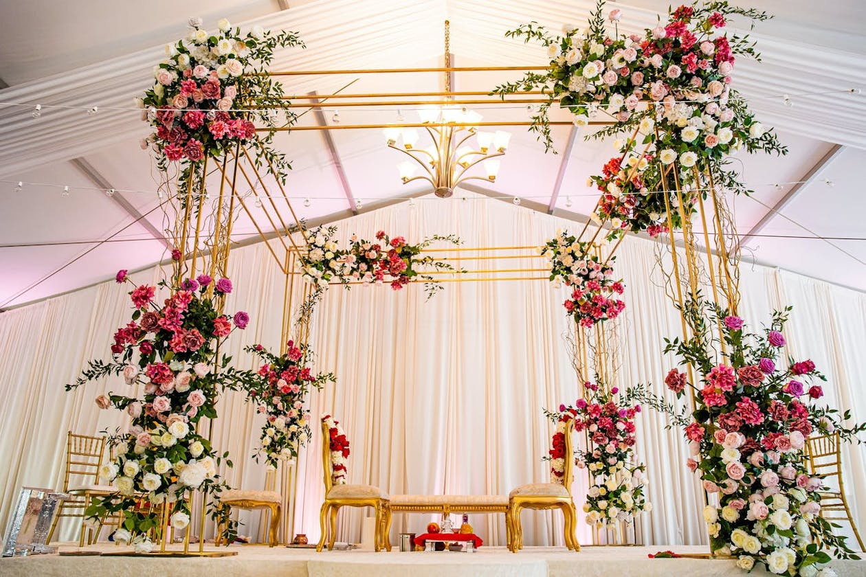 Modern gold Indian wedding mandap structure with bold pink flowers and touches of greenery | PartySlate