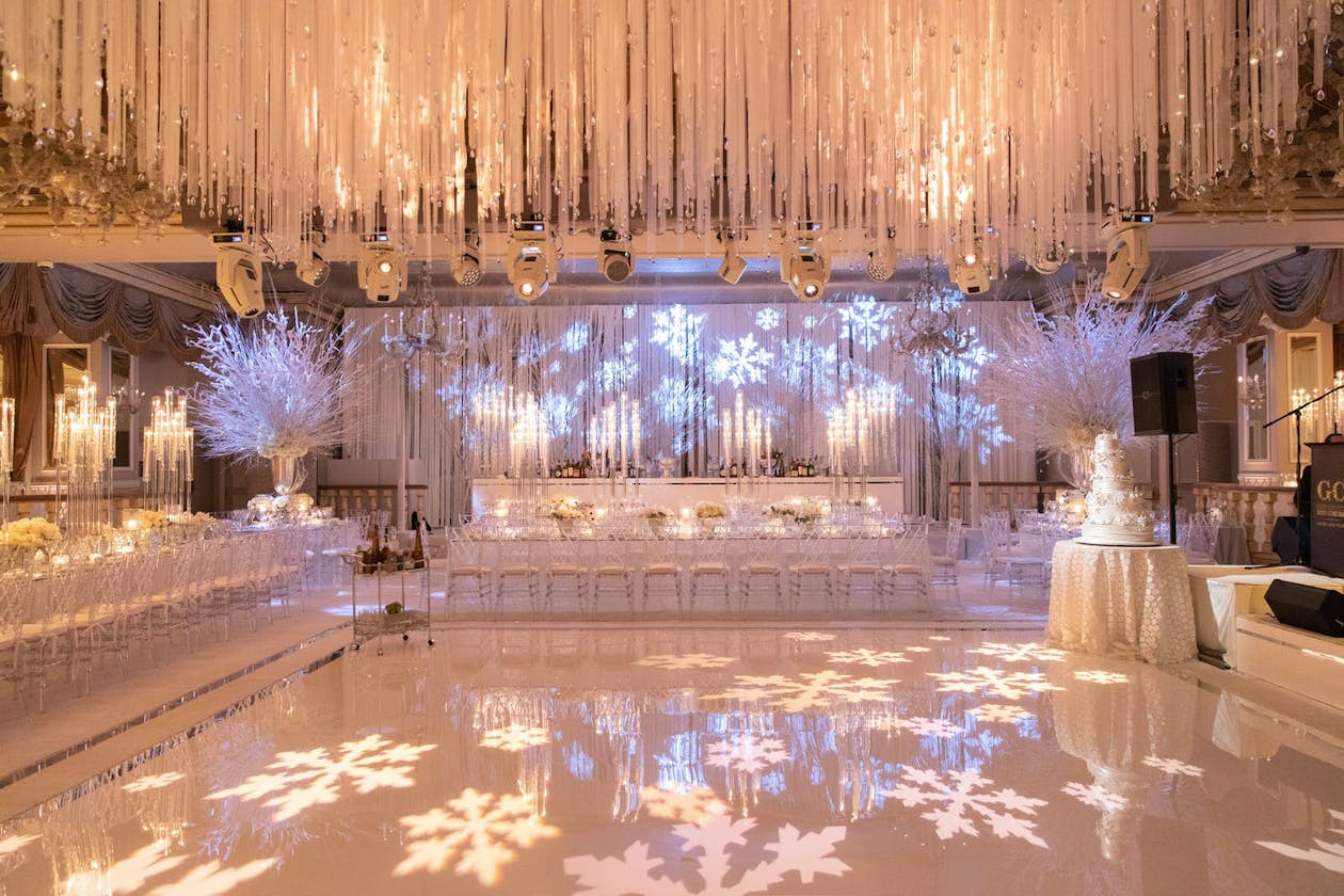 Wedding winter wonderland dance floor with suspended white floral ceiling décor and snowflake lighting projections on wall and dance floor | PartySlate