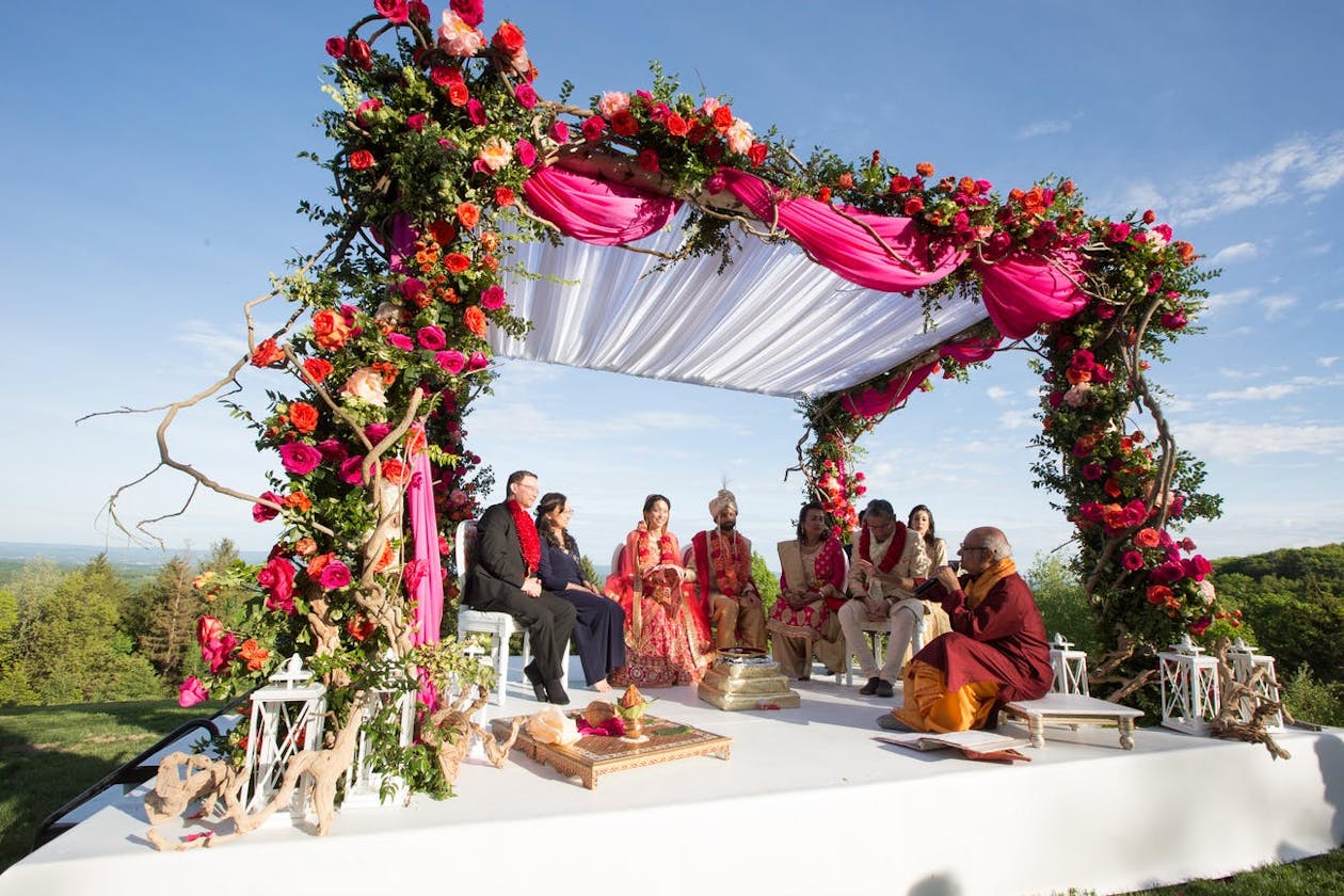 Wedding mandap with lavish greenery and blooms and bright pink drapery | PartySlate