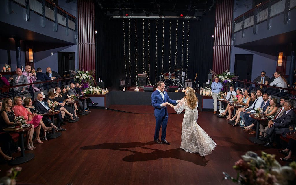 Couple dance to first song at Mayne Stage with friends seated around them on dance floor | PartySlate