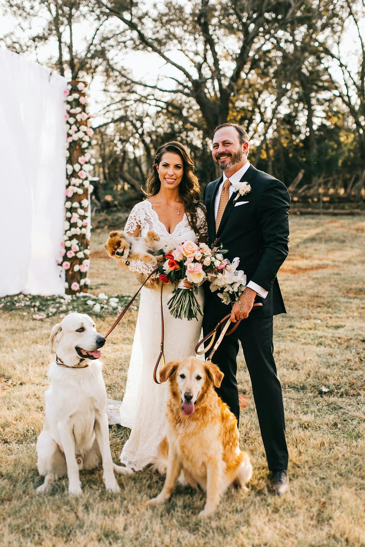 bride and groom posing with two dogs on leashes | PartySlate