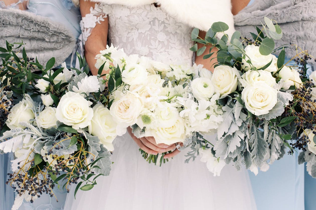 Winter bride and two bridesmaids hold white winter bouquets | PartySlate