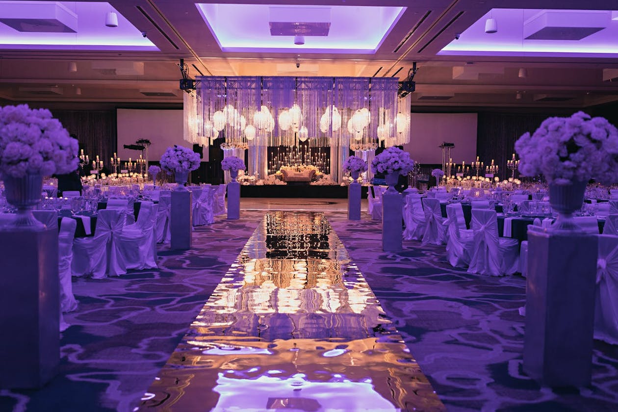 Ultra luxe Indian wedding reception with mirrored aisle, purple uplighting, and wedding stage with geometric lighting and suspended fringe | PartySlate