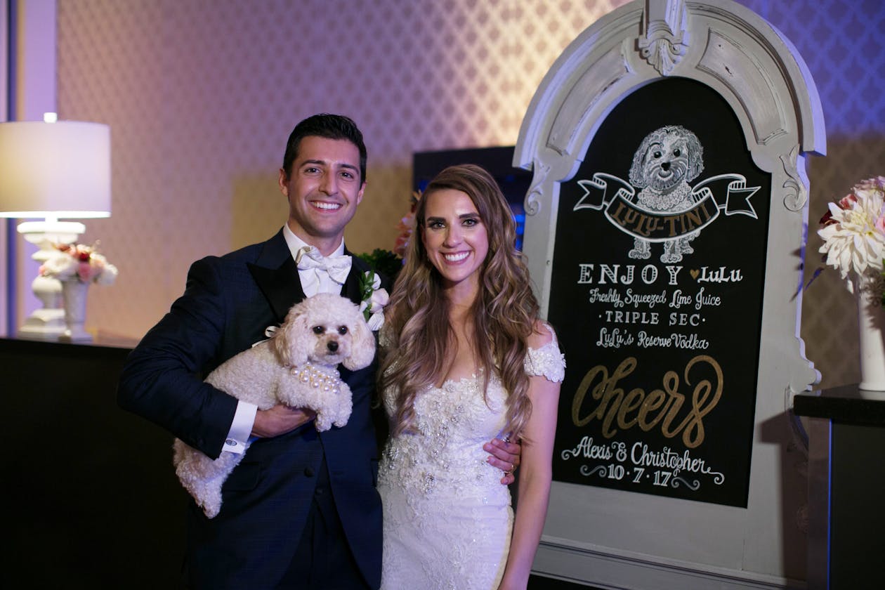 wedding couple holding dog in front of signature cocktail sign | Partyslate