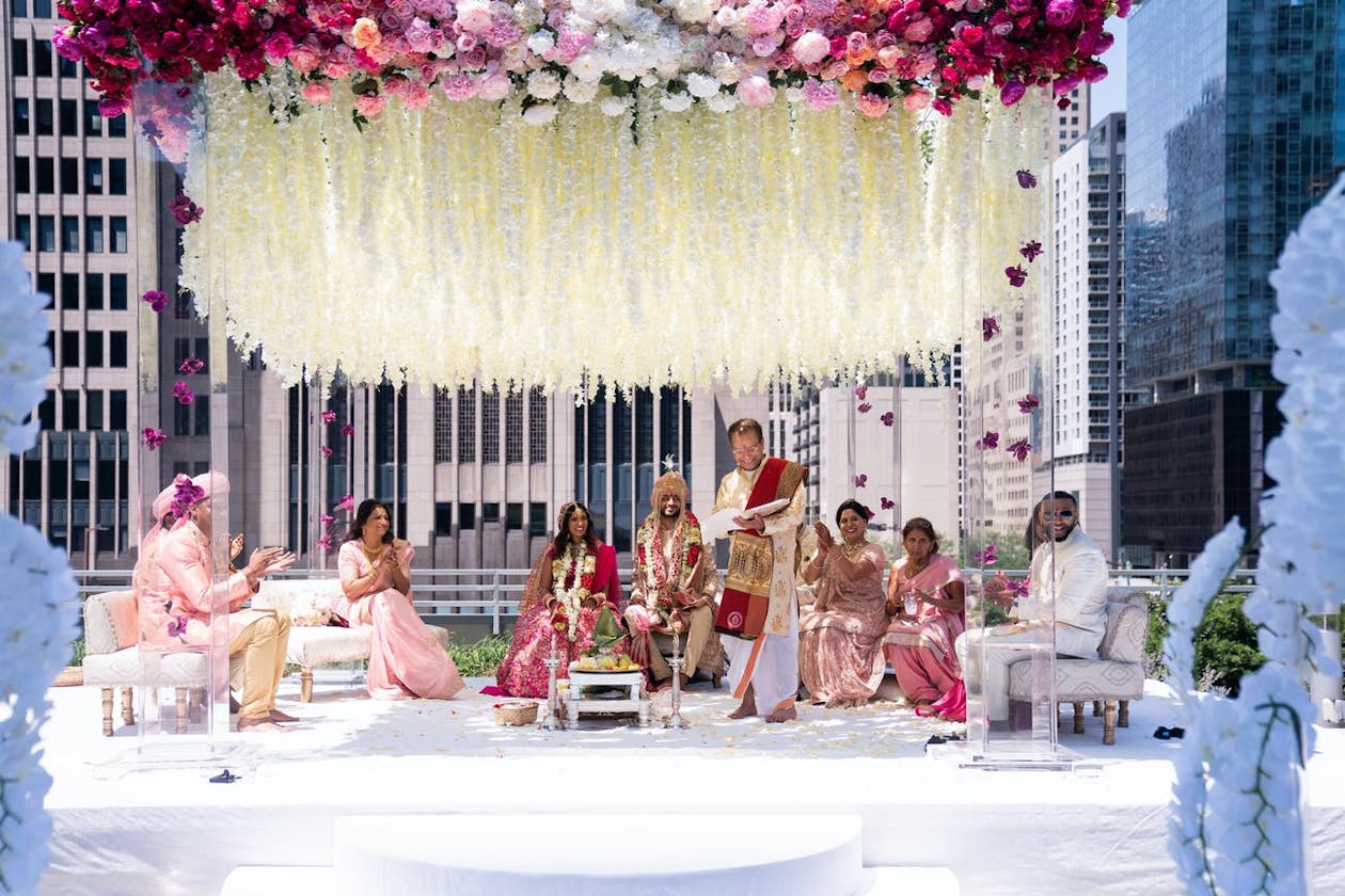 Lucite wedding mandap with pink floral canopy and suspended white floral fringe | PartySlate