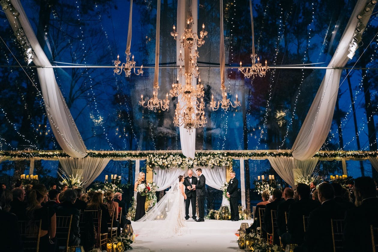 Transparent tented winter wedding with several suspended glimmering gold chandeliers | PartySlate