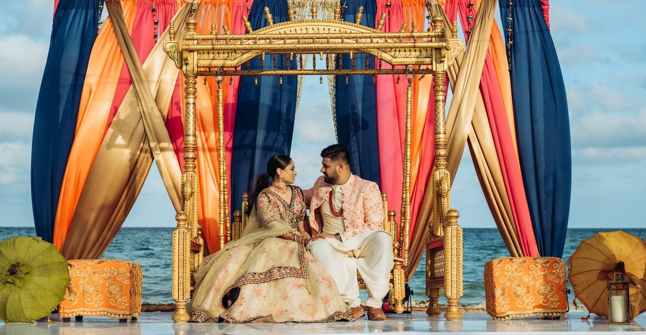 Jhula beneath a mandap of blue, gold, and peach drapery at Indian wedding | PartySlate