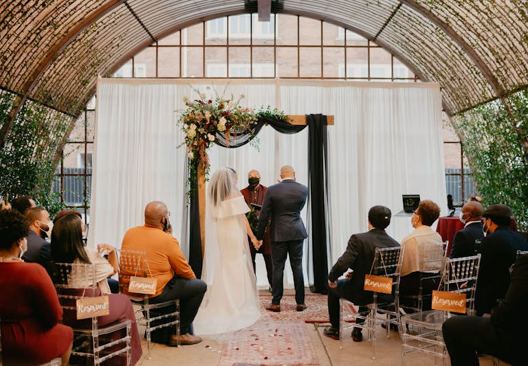 Wedding Ceremony at Ronin Art House in Houston With Couple at Alter and Windows Behind | PartySlate