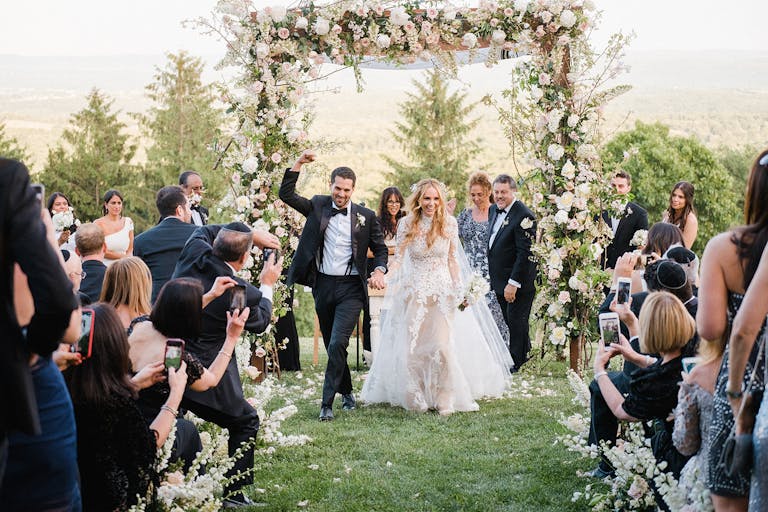Bright Wedding at Cedar Lakes Estate in Hudson Valley New York With Couple Walking Back Down Aisle With Floral Arch Behind Them | PartySlate