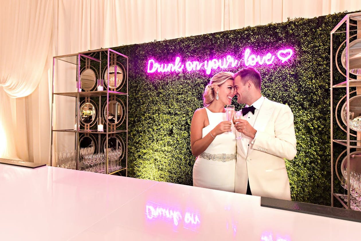Wedding Bar with Cute Pink Neon Sign And Couple Making A Toast | PartySlate