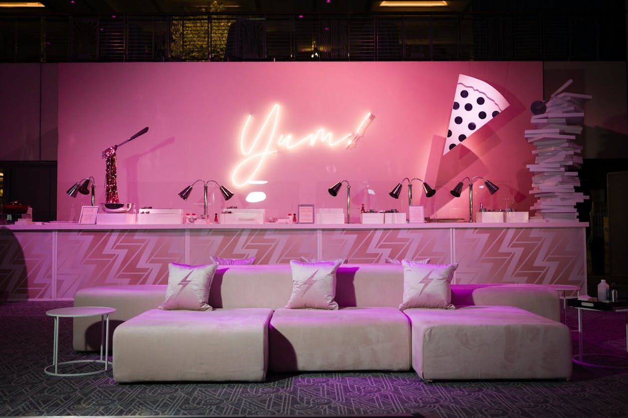 Neon Yum Sign on Pink Backdrop Behind Bar With Couches | PartySlate