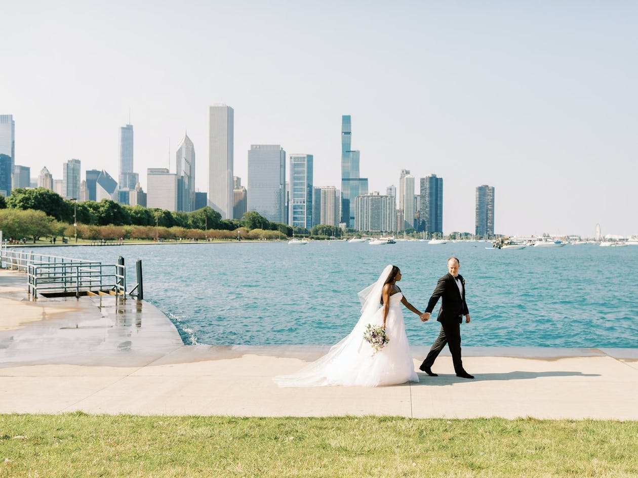 bride and groom hold hands and walk along lake michigan with Chicago in background