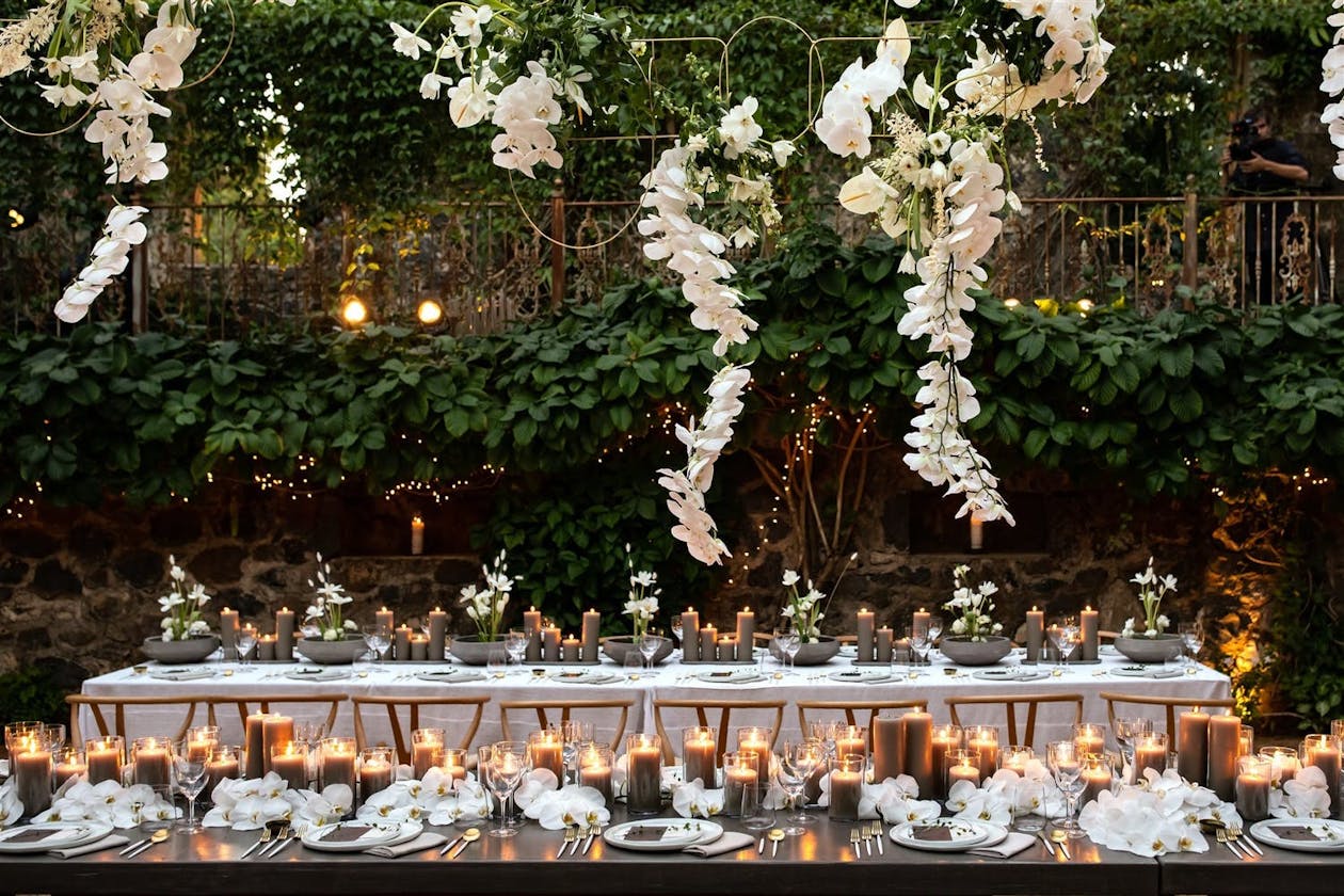 Outdoor wedding in Maui with lots of greenery and suspended white orchids over tabletops | PartySlate